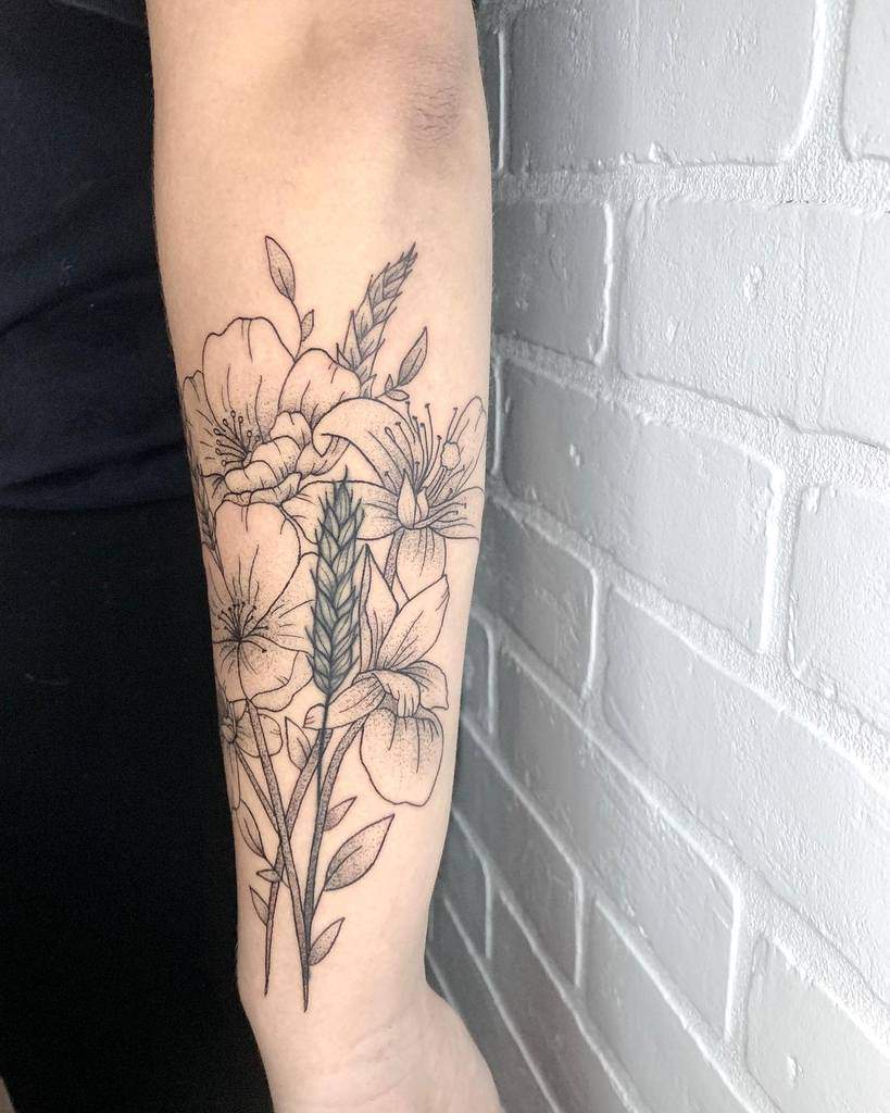 Delicate forearm tattoo featuring detailed wildflowers, leaves, and a wheat sprig in fine black ink for a natural aesthetic