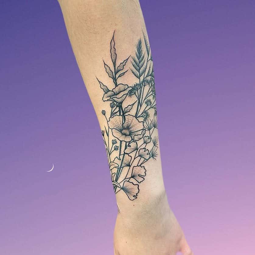 Intricate forearm tattoo of wildflowers, leaves, and stems in fine black ink, showcasing a graceful botanical design