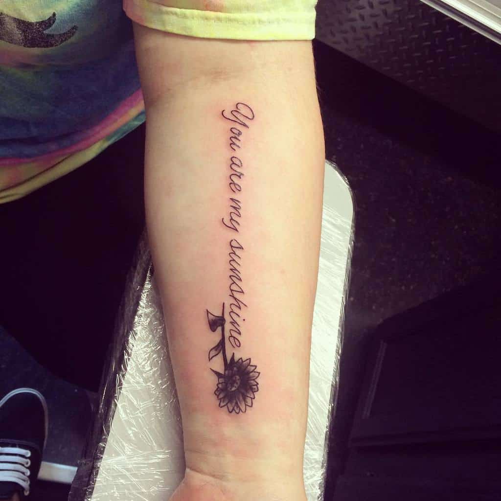 Tattoo on forearm: "You are my sunshine" with a sunflower design below the text