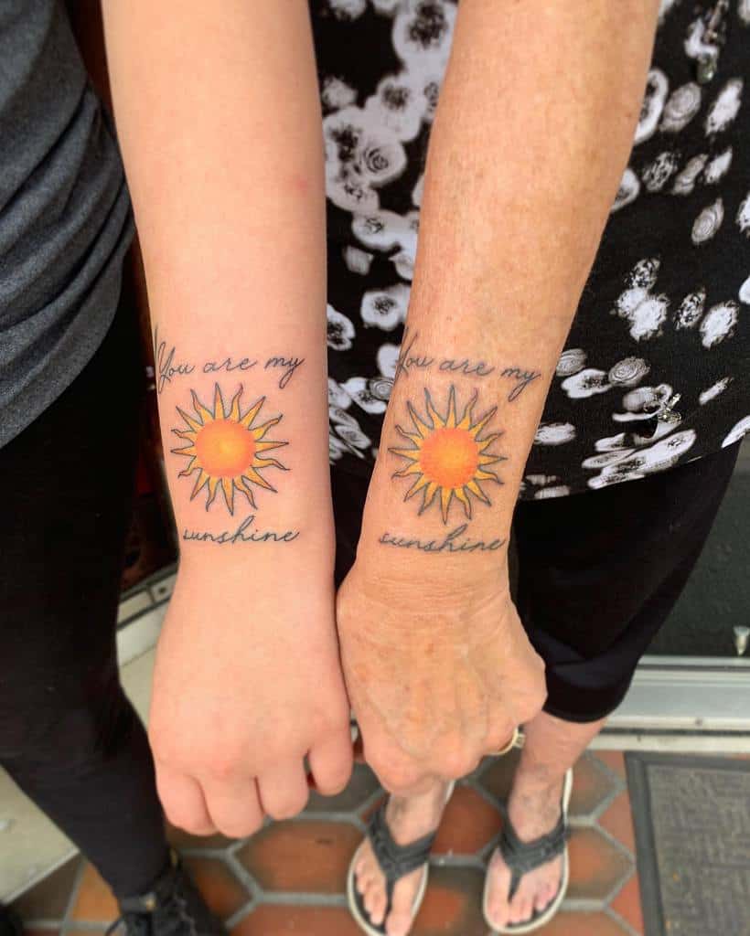 Two arms with matching sun tattoos and the phrase "You are my sunshine"