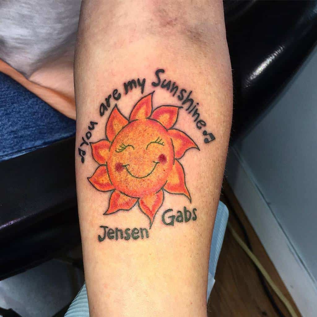 Tattoo of a smiling sun with "you are my Sunshine" and names "Jensen" and "Gabs"
