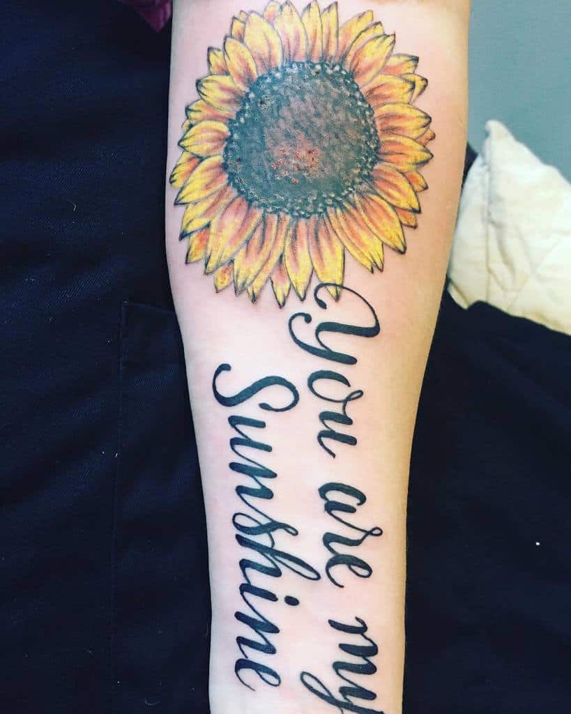 Tattoo of a sunflower and "You are my Sunshine" on a forearm