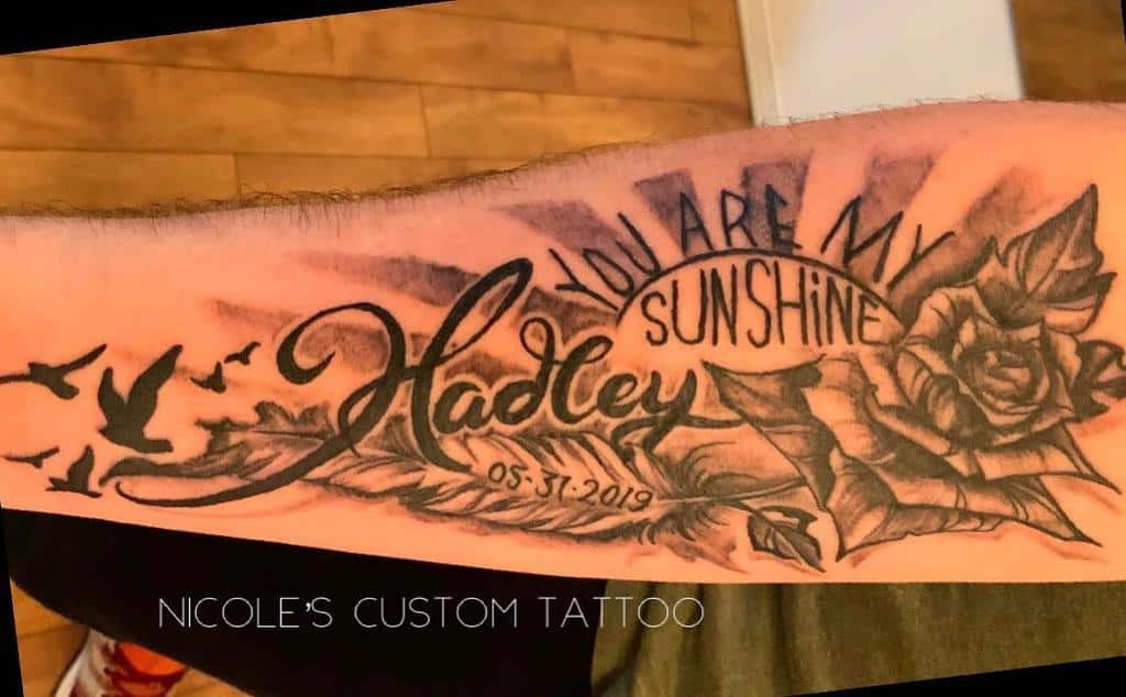 Forearm tattoo with 'You are my sunshine,' a name, date, rose, birds, and sunray details in black and grey shading