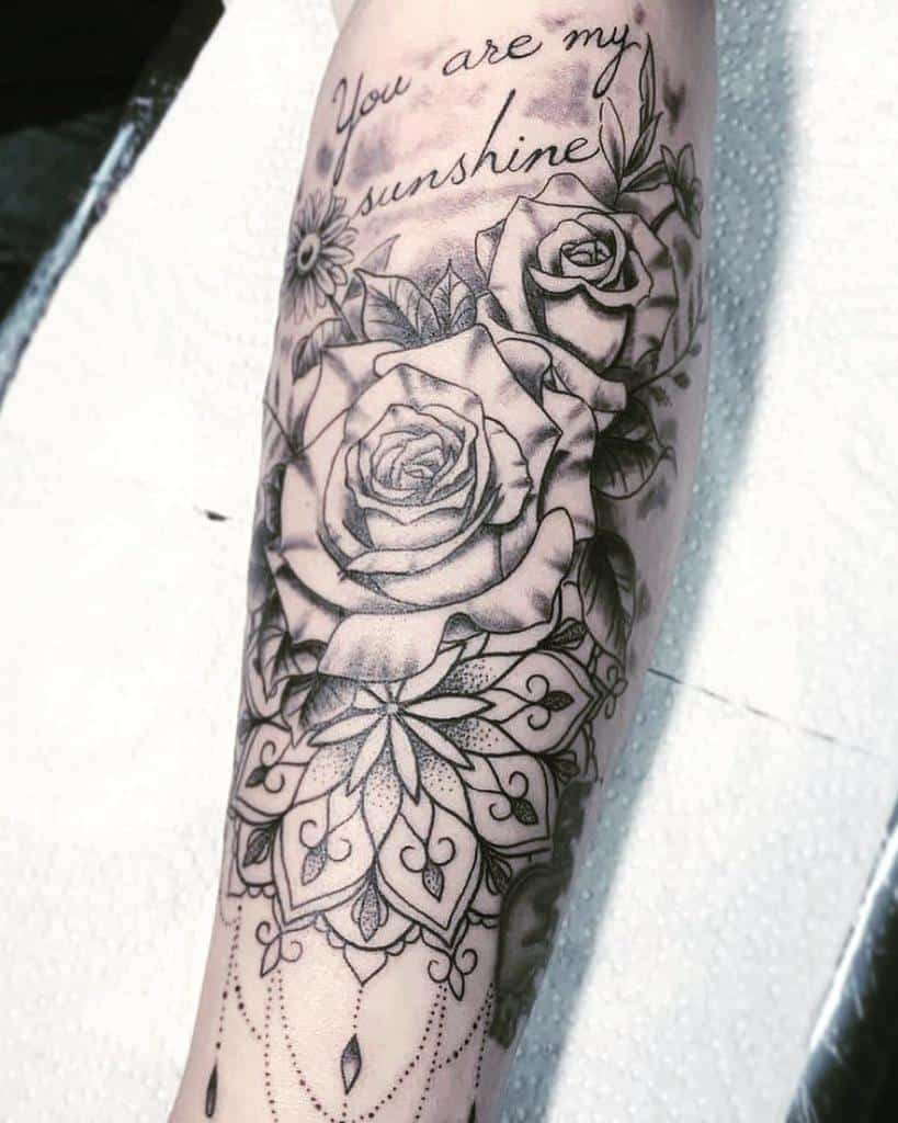 Intricate forearm tattoo with 'You are my sunshine,' detailed roses, and a mandala design in black and grey shading