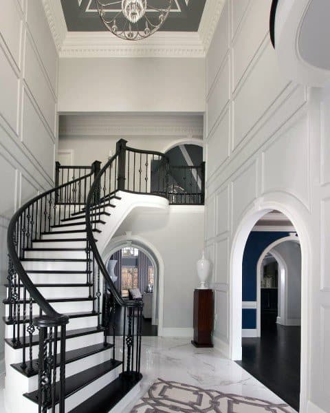Elegant interior with a grand staircase featuring black railings, white walls, and arched doorways