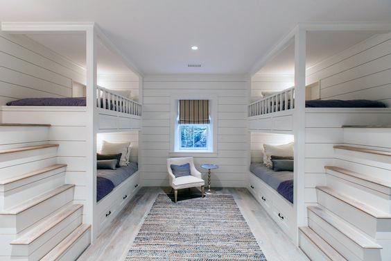 Cozy room with four bunk beds, a central chair, small table, and window overlooking a woven rug on the floor