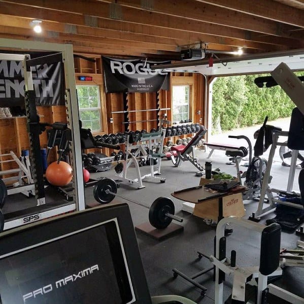 Spacious garage gym with dumbbell rack, cardio equipment, weight benches, and wooden interior.