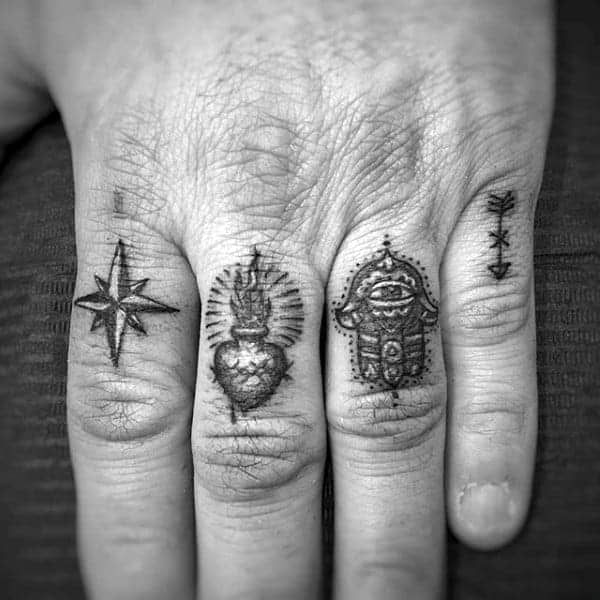 Fingers with four small tattoos: a star, heart, hamsa, and arrow symbols