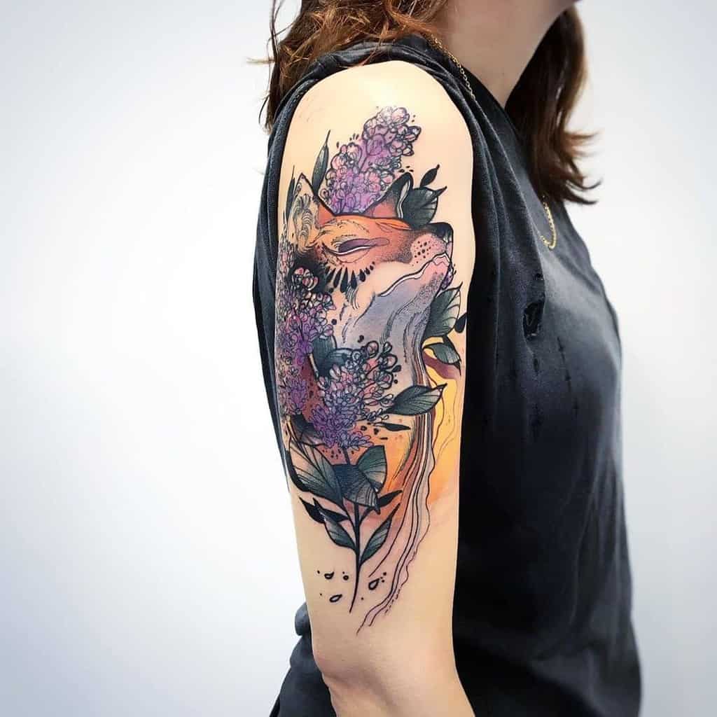 Stunning upper arm tattoo of a fox intertwined with lilac flowers and dark leaves, featuring bold colors and artistic shading.