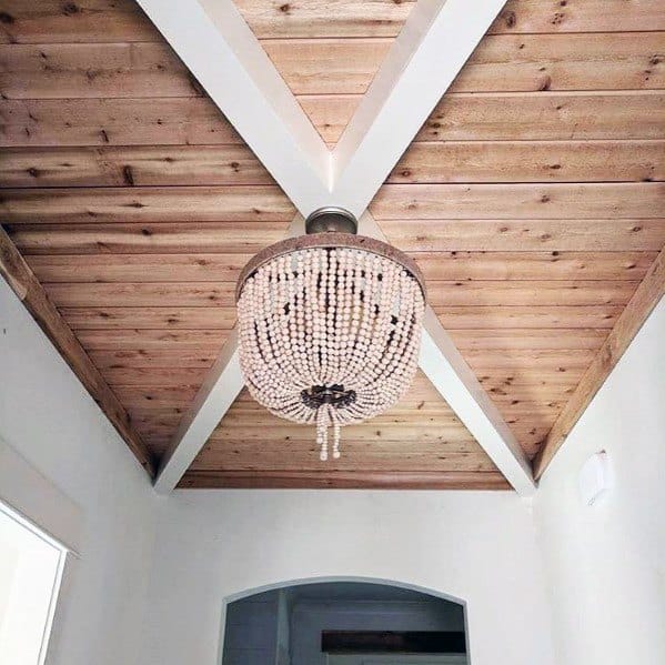 Rustic wood plank ceiling with white beams and a beaded chandelier in a cozy foyer.