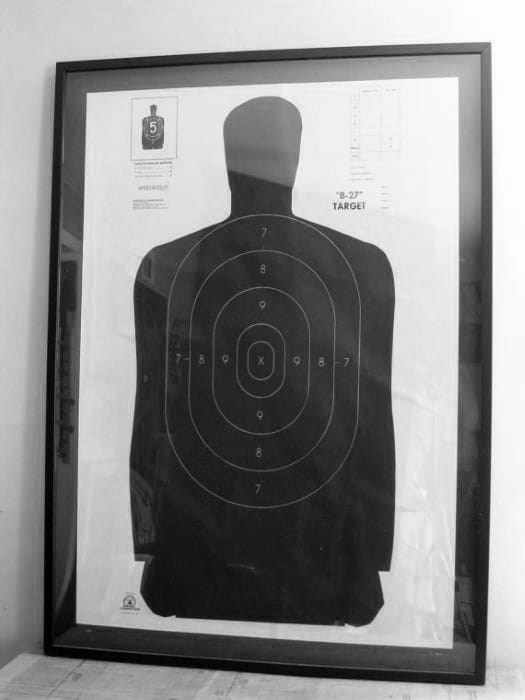 Framed black and white shooting target with silhouette and scoring rings displayed on a wall