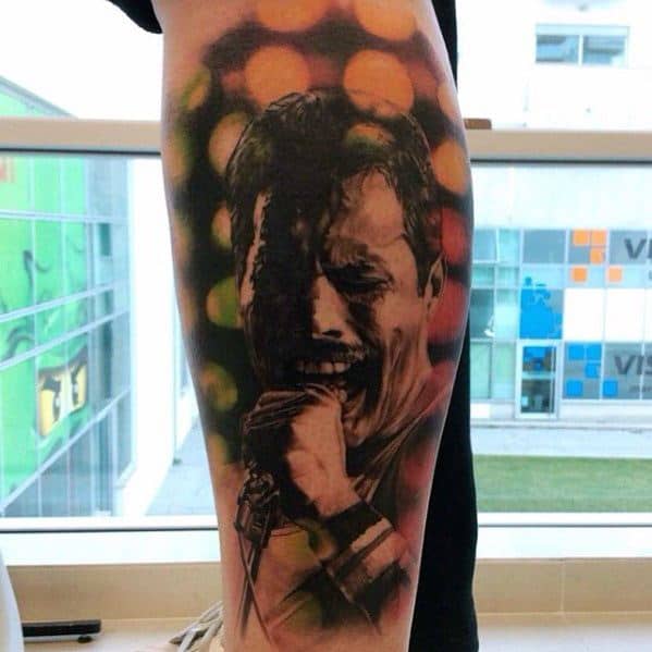 Bold Freddie Mercury tattoo in black and grey with vibrant bokeh-style lights in the background, capturing an emotional stage moment.