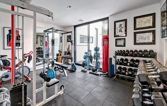 Bright home gym with weights, machines, and fitness gear; framed photos adorn the room