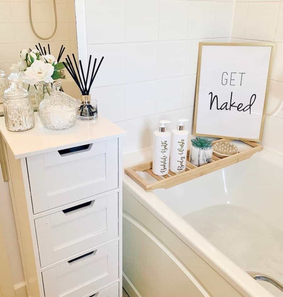 Cozy bathroom with small white cabinet, bathtub tray, and "Get Naked" wall art.