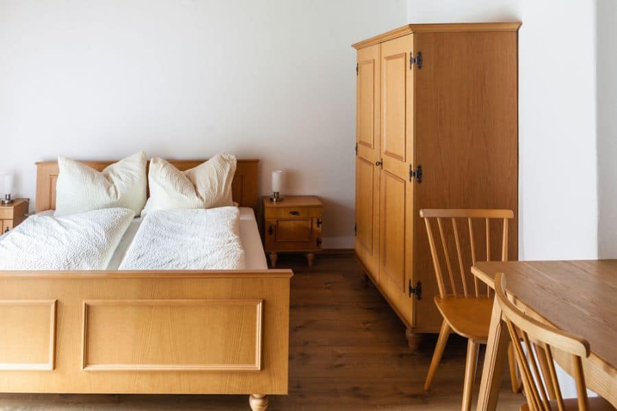 Wooden bedroom set with bed, freestanding cabinet, and wooden chairs.