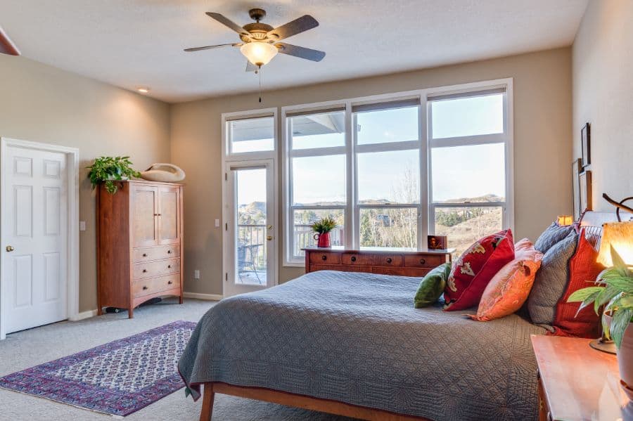 Spacious bedroom with large windows, wooden bed, dresser, and ceiling fan.