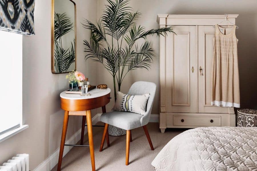 Elegant bedroom with freestanding cabinet, vanity table, and indoor plant.