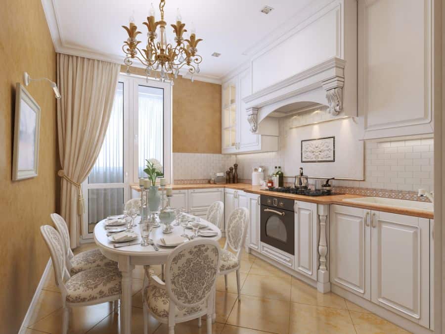 Elegant french country kitchen with white cabinets ornate chandelier and round dining table.