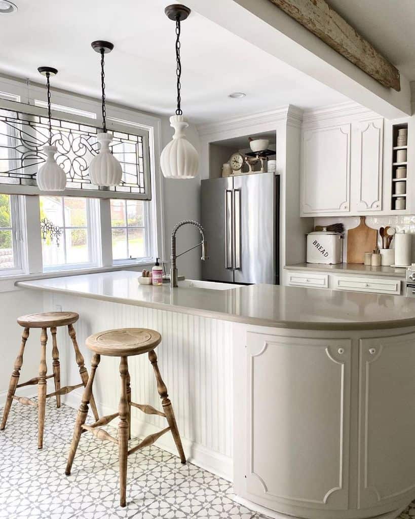 Bright french country kitchen with curved island wooden stools and vintage pendant lights.