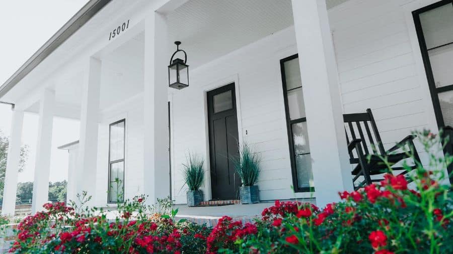 large white home with black front door and red flower bed