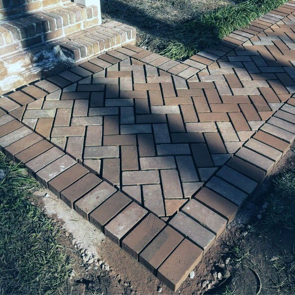 Brick walkway with a herringbone pattern, bordered by grass and dirt