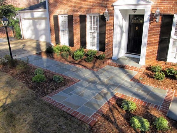Stylish front yard with a flagstone walkway bordered by brick, leading to a classic front door with decorative lamps