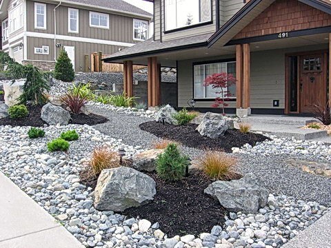 Front yard with river rock landscaping, featuring a mix of large rocks, gravel, plants, and a well-maintained pathway leading to the house