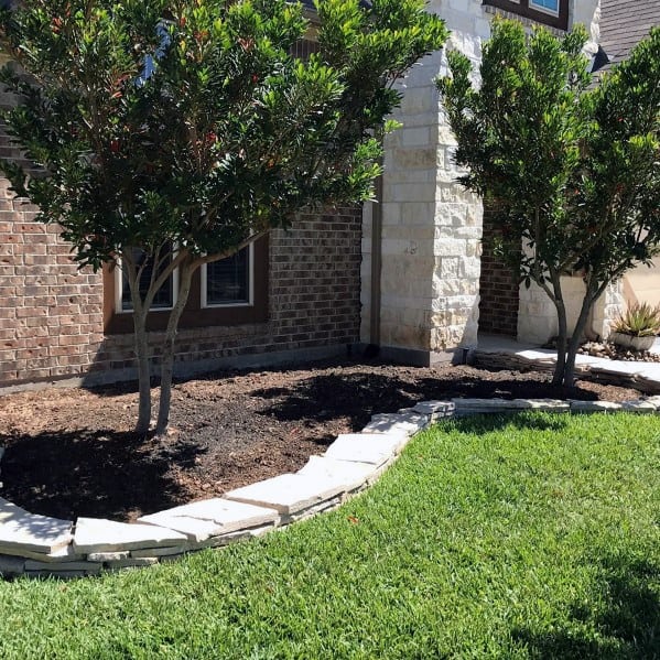 Stone edging outlining a landscaped garden with trees and fresh grass in the front yard of a house