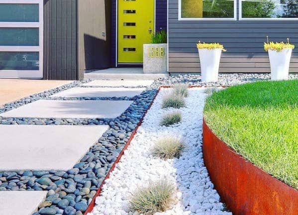 Modern front yard with contrasting black and white river rock landscaping, geometric concrete slabs, and vibrant green grass