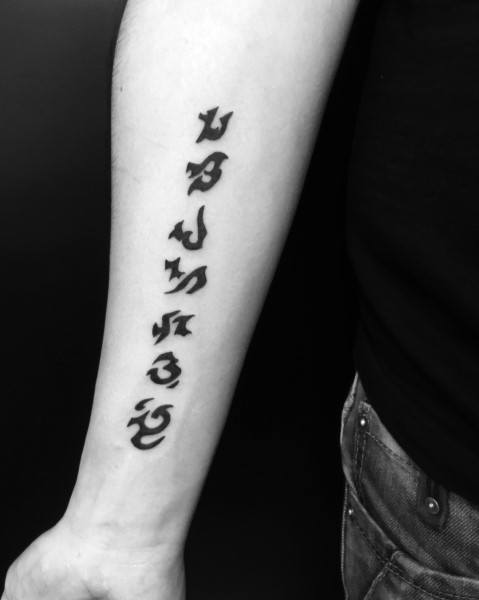 Black ink tattoo of Warcraft runes vertically aligned on a forearm, featuring bold, stylized lettering inspired by the game's fantasy script.
