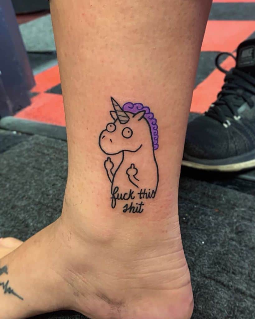 Funny tattoo of a grumpy unicorn with a purple mane, flipping both middle fingers, with 'f*** this s***' written below in casual script.