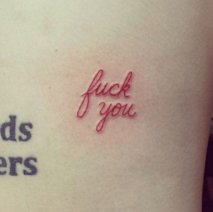 Funny tattoo of 'f*** you' in delicate cursive, inked in a soft red, blending elegance with attitude in a minimalist design.