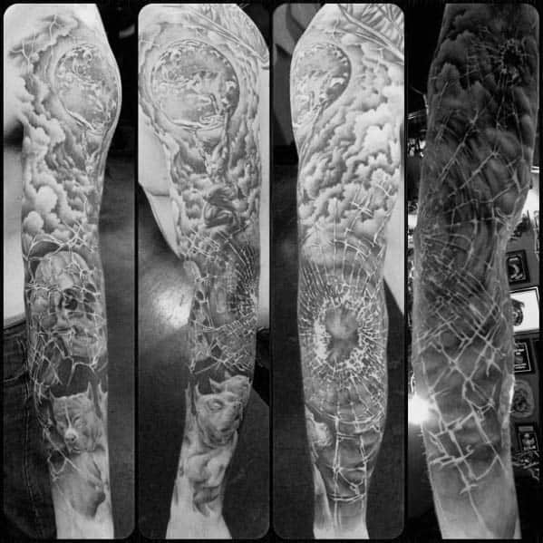 Full sleeve tattoo in black and grey featuring shattered glass patterns, skulls, and celestial elements blending into a dramatic surreal design.