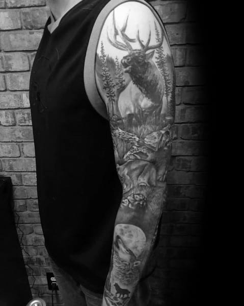 Realistic black and grey wildlife sleeve tattoo featuring an elk, wolf, and forest landscape, creating a bold and nature-inspired design.