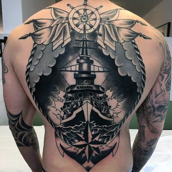 Large black and grey battleship tattoo spanning the entire back, featuring a detailed warship with stormy waves, a compass rose, and winged banners surrounding a ship's wheel at the top