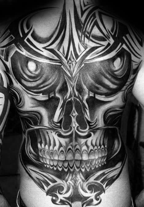Massive full-back tribal skull tattoo with bold symmetrical patterns, dark shading, and fierce teeth forming a dramatic visual impact.