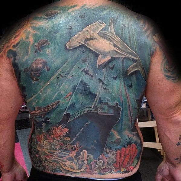 Full back tattoo of an underwater shipwreck scene featuring a hammerhead shark, sea turtles, coral reef, and sunken vessels.