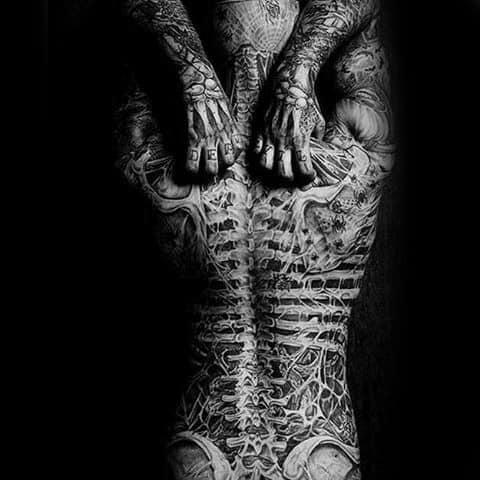 Black and white photo of a heavily tattooed back and hands with intricate designs