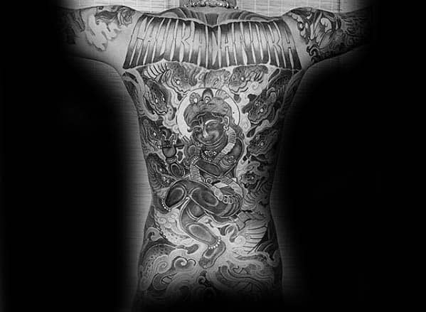 Dramatic black and grey full-back Krishna tattoo showing Krishna seated with a flute, surrounded by swirling clouds, divine energy, and mythical creatures.