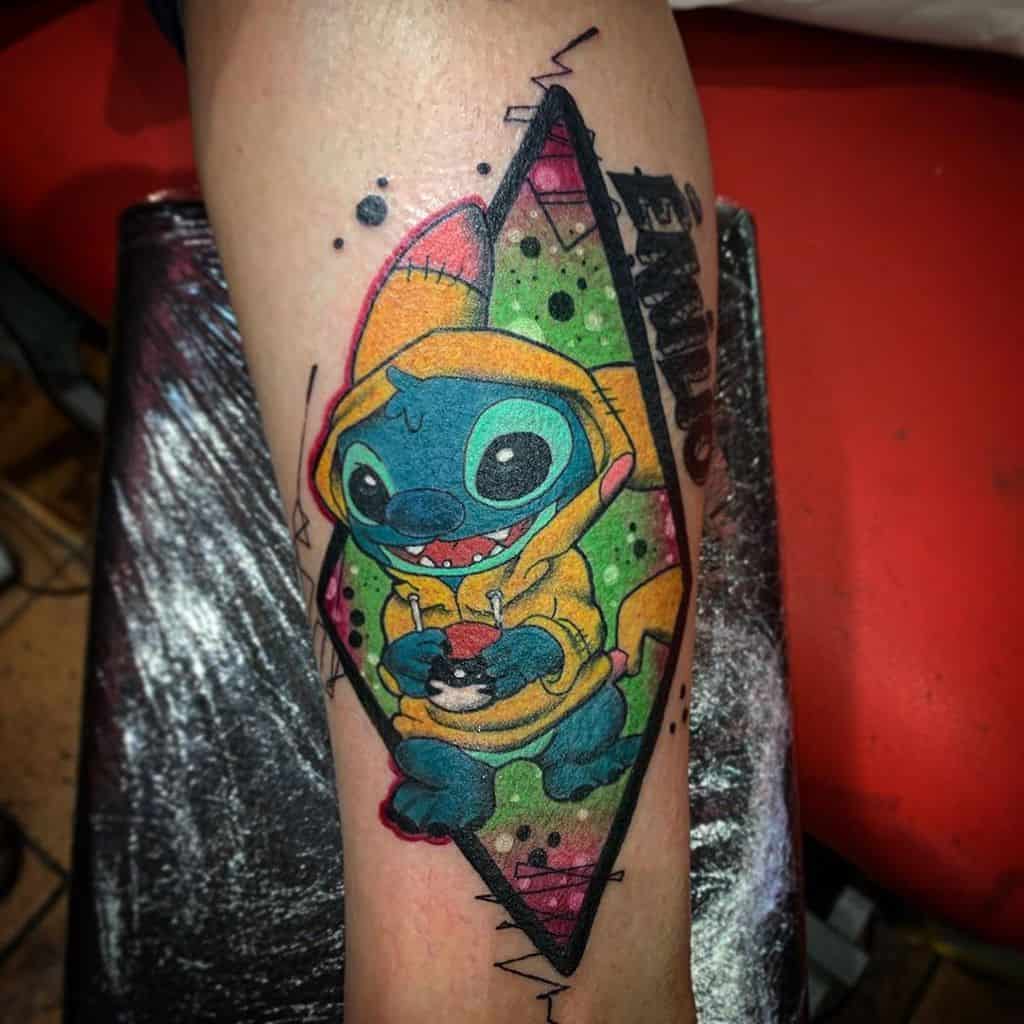 Colorful tattoo of Stitch from Lilo & Stitch wearing a yellow hoodie, holding a Pokéball, with a vibrant geometric background and bold lines, on the forearm.