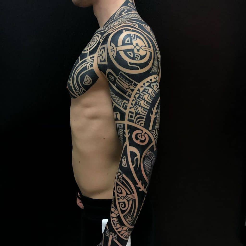 Man with intricate black geometric tribal tattoos covering chest, arm, and shoulder