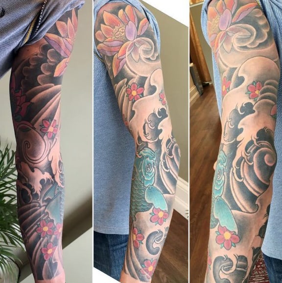 Japanese-style full sleeve tattoo featuring soft shading, pink cherry blossoms, swirling clouds, a lotus flower, and intricate wave patterns
