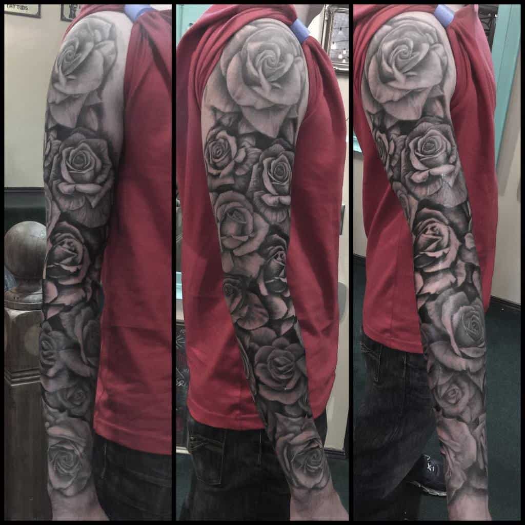 A full sleeve tattoo adorns the arm, featuring intricately detailed black and gray roses