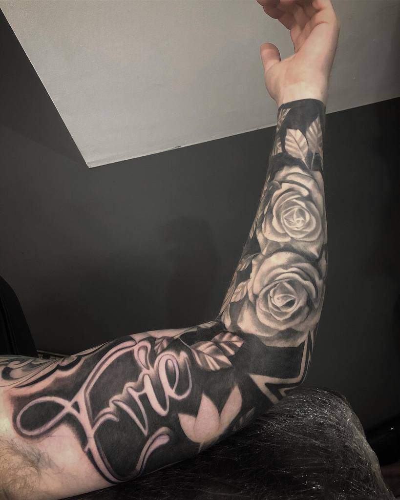 A full sleeve tattoo with a combination of roses and flowing script, featuring intricate shading and detailed textures that blend floral elements with soft gradients