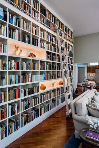 Tall bookshelf with a sliding ladder, filled with books and some decorations, in a cozy living room with a sofa