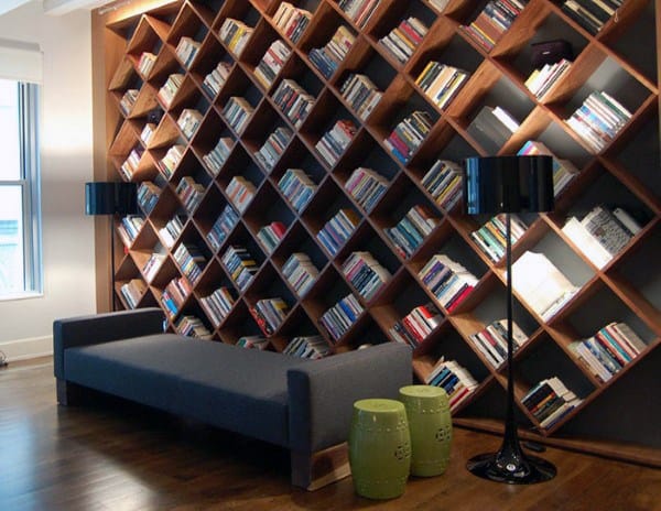 Diagonal bookshelf with books, gray couch, two black lamps, and green stools in a cozy room