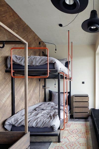 A modern room with wooden walls features cozy bedding and a patterned rug under the bunk beds