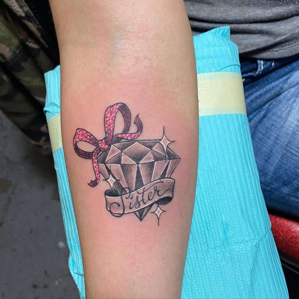 Sister tattoo featuring a sparkling diamond wrapped in a pink ribbon, with a banner reading 'Sister,' symbolizing a precious sibling bond