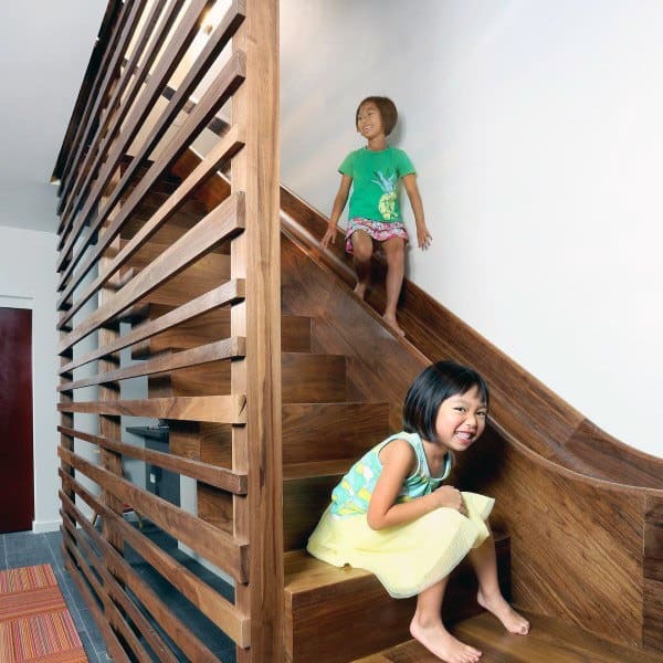 Two children play on a wooden staircase, smiling and sitting as if ready to slide down the steps