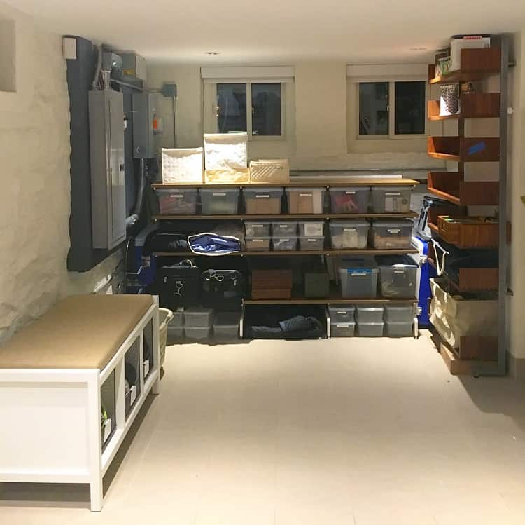 Basement with functional shelves and labeled storage bins, along with a cushioned bench for seating.